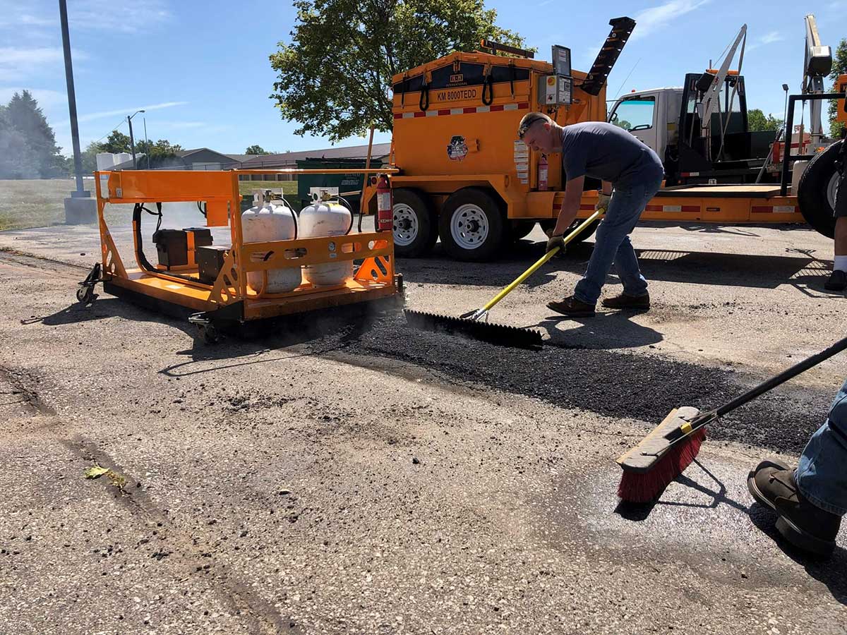 A road maintenance professional uses an asphalt lute.